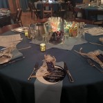 Blue linens on table with menus and table settings. Jars of crayons, glow sticks, and sunglasses are on the table.