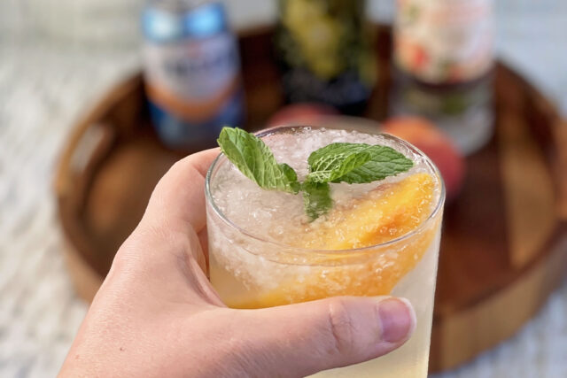 This peach and orange blossom sangria is served over crushed ice and topped with mint and a sliced peach.