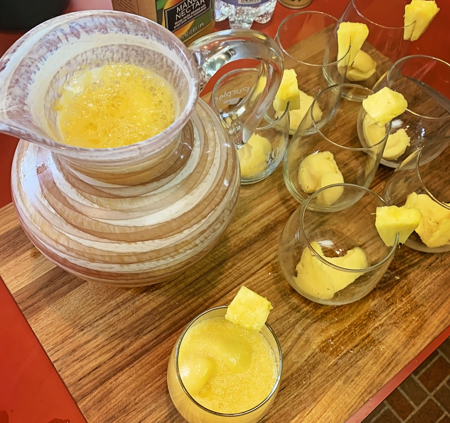 Mango and Pineapple Non-Alcoholic Punch served in a pitcher with prepped glasses filled with mango sorbet and garnished with pineapple.