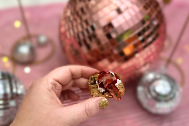 Cranberry Prosciutto Goat Cheese Appetizer held in front of sparkly pink and silver mirror balls