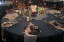 Blue linens on table with menus and table settings. Jars of crayons, glow sticks, and sunglasses are on the table.