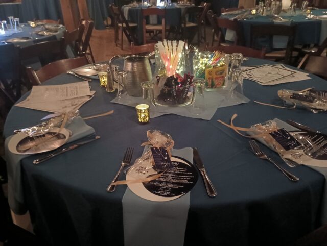 Blue linens on table with menus and table settings. Jars of crayons, glow sticks, and sunglasses are on the table.