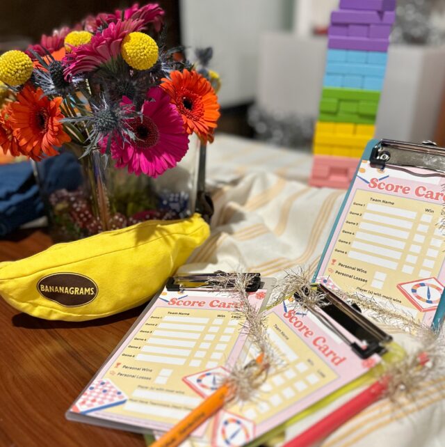 game night score cards on clip boards with pencils attached, bright flowers and games in background.