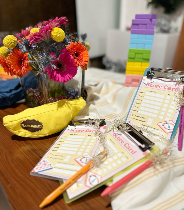 Score cards on mini clipboards with pencils attached. Flowers and games in background.